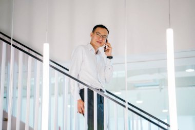 Modern ofis adımlarla yürürken telefonda konuşan Asyalı adam