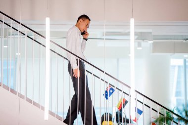 Yürürken telefonda konuşan Asya adam modern ofis, tam uzunlukta adımlar
