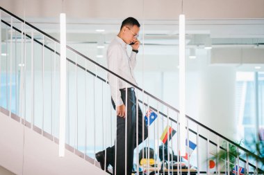 Yürürken telefonda konuşan Asya adam modern ofis, tam uzunlukta adımlar