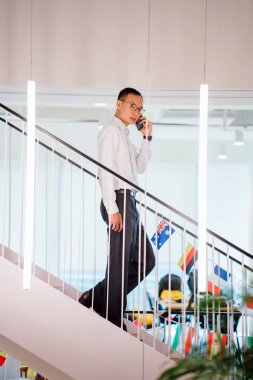 Yürürken telefonda konuşan Asya adam modern ofis, tam uzunlukta adımlar