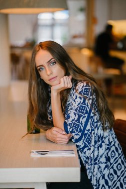 Kafede oturan ve kameraya bakarak uzun saçlı genç çekici kadın portresi