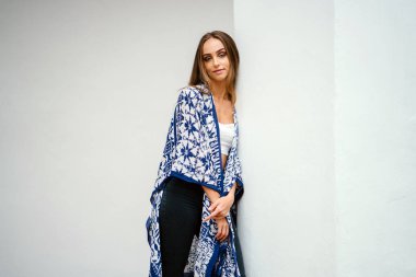 Beyaz duvara yaslanmış ve kameraya gülümseyen poz genç çekici kadın portresi.