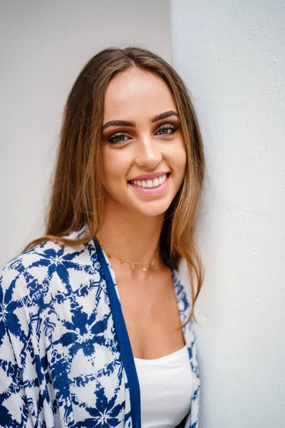 Beyaz duvara yaslanmış ve kameraya gülümseyen genç güzel kız portresi.