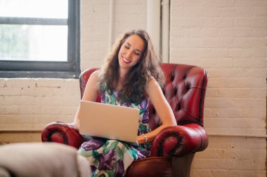 Kırmızı koltuk kafede oturan ve dizüstü bilgisayarda çalışan bir genç işkadını yorgun