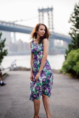 mutlu kadın kıvırcık saçlı riverside Köprüsü arka plan üzerinde yürürken