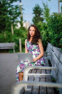 yeşil parkta bankta oturmuş dizüstü bilgisayar ile esmer kadın