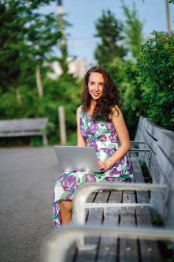 yeşil parkta bankta oturmuş dizüstü bilgisayar ile esmer kadın