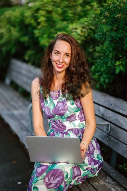yeşil parkta bankta oturmuş dizüstü bilgisayar ile gülümseyen esmer kadın