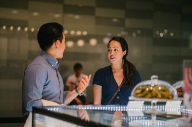  Genç Çinli Asyalı Çift kek bir perakende alışveriş merkezinde bir görüntüsünü düşünüyor. Onlar bir hafta sonu bir tarihte tatlılar sahip düşünüyor musun.