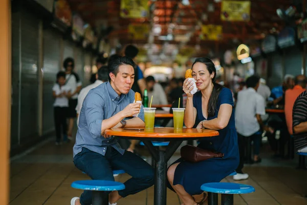 Portrait of a good looking Chinese Asian couple enjoying a snack at a hawker center during the weekend in Singapore, Asia. They are enjoying  sugarcane juice and fried bananas.