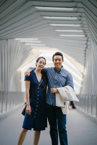 Portrait of an Asian Chinese couple on a date over the weekend. The man is young, handsome and well-dressed and the woman is wearing an elegant summer dress. They are  on a bridge.