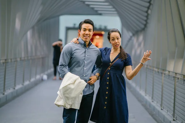 Portrait of an Asian Chinese couple on a date over the weekend. The man is young, handsome and well-dressed and the woman is wearing an elegant summer dress. They are  on a bridge.