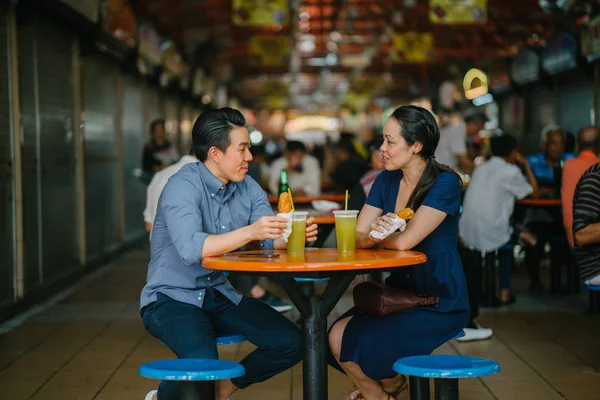 Portrait of a good looking Chinese Asian couple enjoying a snack at a hawker center during the weekend in Singapore, Asia. They are enjoying  sugarcane juice and fried bananas.