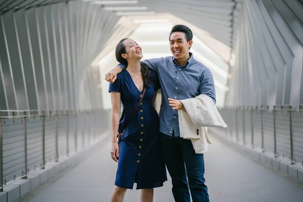 Portrait of an Asian Chinese couple on a date over the weekend. The man is young, handsome and well-dressed and the woman is wearing an elegant summer dress. They are  embracing on a bridge.