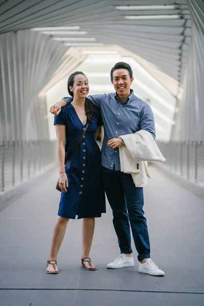 Portrait of an Asian Chinese couple on a date over the weekend. The man is young, handsome and well-dressed and the woman is wearing an elegant summer dress. They are  embracing on a bridge.