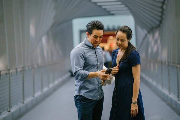 Portrait of an Asian Chinese couple on a date over the weekend. The man is young, handsome and well-dressed and the woman looking for direction in smartphone