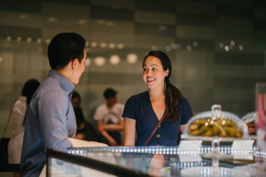  Genç Çinli Asyalı Çift kek bir perakende alışveriş merkezinde bir görüntüsünü düşünüyor. Onlar bir hafta sonu bir tarihte tatlılar sahip düşünüyor musun.