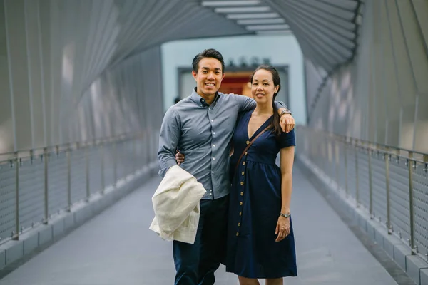 Portrait of an Asian Chinese couple on a date over the weekend. The man is young, handsome and well-dressed and the woman is wearing an elegant summer dress. They are  on a bridge.