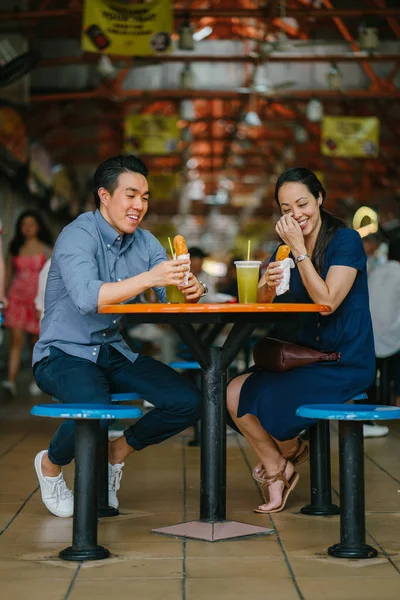 Portrait of a good looking Chinese Asian couple enjoying a snack at a hawker center during the weekend in Singapore, Asia. They are enjoying  sugarcane juice and fried bananas.
