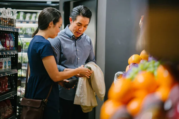 A young Chinese Asian couple shopping  at a supermarket together. They are young, attractive and are smiling as they shop.