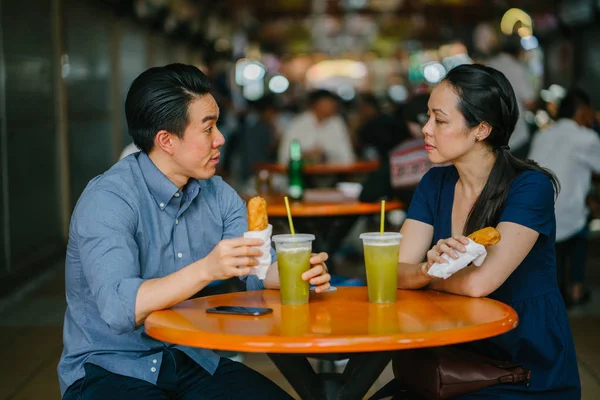 Portrait of a good looking Chinese Asian couple enjoying a snack at a hawker center during the weekend in Singapore, Asia. They are enjoying  sugarcane juice and fried bananas.