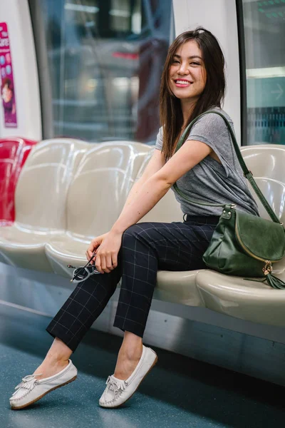 young and pretty Japanese Asian tourist woman sitting on a train in Asia while on vacation. She is cute, attractive and is smiling happily as she relaxes in her seat.