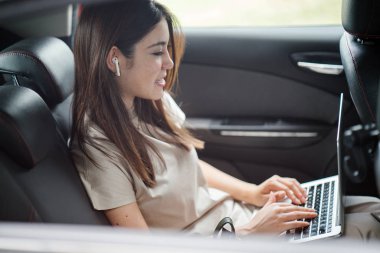 Güzel genç Asyalı kadın arabada dizüstü bilgisayar kullanarak 