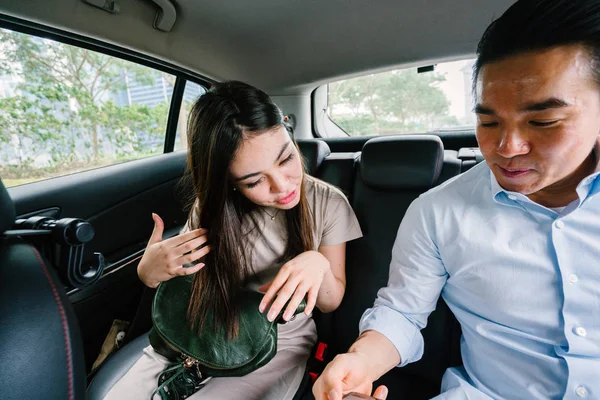 Two young Asian business people sit on the back seat of a car and are driven to their destination on a ride they booked via a ride hailing app.