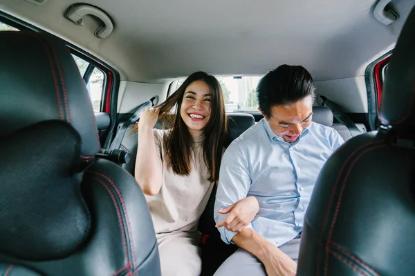 Two young Asian business people sit on the back seat of a car and are driven to their destination on a ride they booked via a ride hailing app.