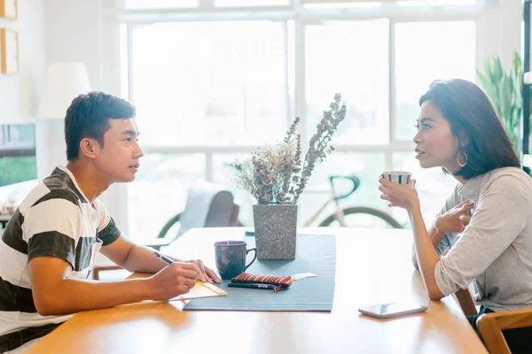 A young married Malay couple enjoying  their morning coffee together in the morning before they go to work. They are talking to one another over coffee in their cosy flat together.