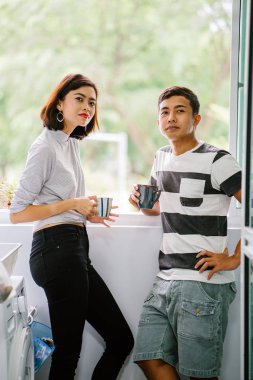 Sıcak bir içecek zevk ve bir başkasına severek konuşurken genç Malay Asya çift. Onlar pencere balkon tarafından gün boyunca birlikte ihale bir an paylaşıyorsunuz.