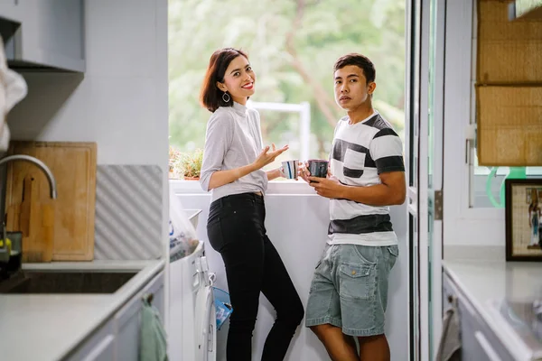 Young Malay Asian couple enjoying a hot drink and talking to one another fondly. They are sharing a tender moment together during the day by the window balcony.