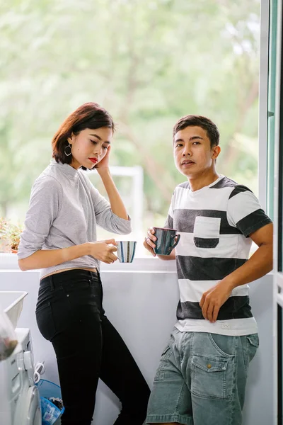 Sıcak bir içecek zevk ve bir başkasına severek konuşurken genç Malay Asya çift. Onlar pencere balkon tarafından gün boyunca birlikte ihale bir an paylaşıyorsunuz.