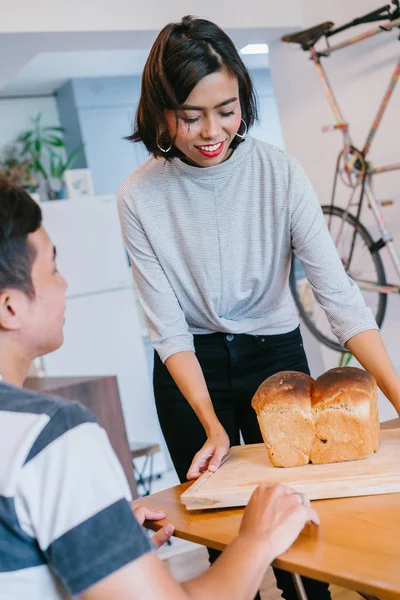 A young Malay woman bakes bread for her husband and serves the freshly baked bread to him on a wooden tray on the weekend