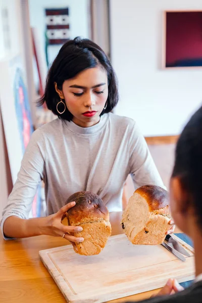 A young Malay woman bakes bread for her husband and serves the freshly baked bread to him on a wooden tray on the weekend