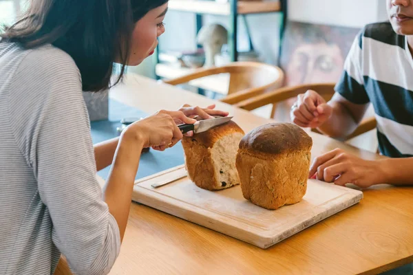 A young Malay woman bakes bread for her husband and serves the freshly baked bread to him on a wooden tray on the weekend