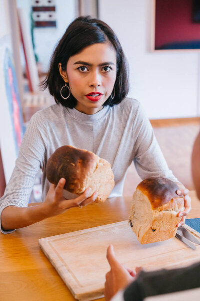 A young Malay woman bakes bread for her husband and serves the freshly baked bread to him on a wooden tray on the weekend