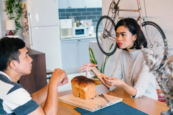 A young Malay woman bakes bread for her husband and serves the freshly baked bread to him on a wooden tray on the weekend