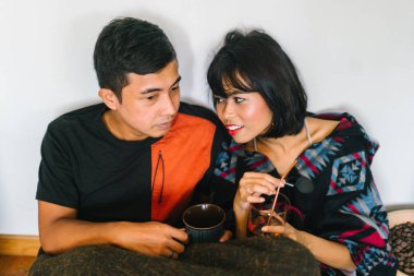 Genç bir Malay çift yatmak ve evlerinde sıcak bir içecek paylaşın. Onlar sarılır up ve birbirleriyle konuşmak gibi zemin ve rahat oturan.