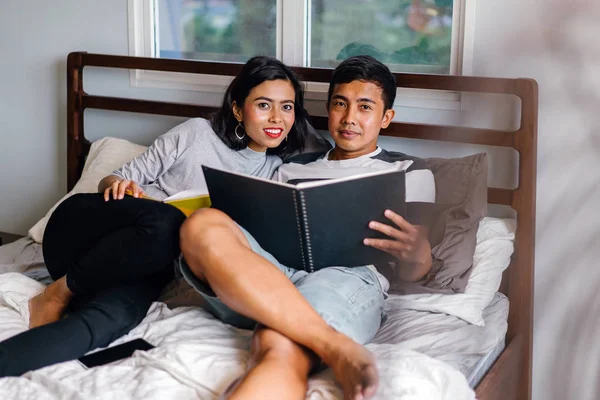 Tembel hafta sonu yatakta oturup bir genç ve çekici Malay Asya çift portresi. 