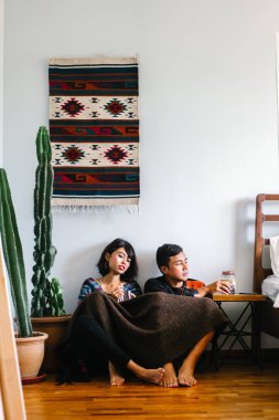 Genç bir Malay çift yatmak ve evlerinde sıcak bir içecek paylaşın. Onlar sarılır up ve birbirleriyle konuşmak gibi zemin ve rahat oturan.