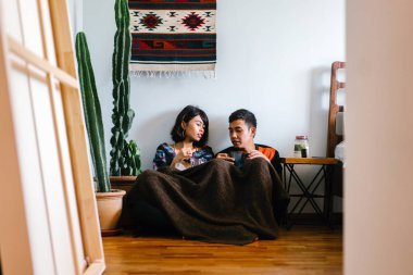 Genç bir Malay çift yatmak ve evlerinde sıcak bir içecek paylaşın. Onlar sarılır up ve birbirleriyle konuşmak gibi zemin ve rahat oturan.