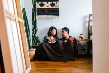 Genç bir Malay çift yatmak ve evlerinde sıcak bir içecek paylaşın. Onlar sarılır up ve birbirleriyle konuşmak gibi zemin ve rahat oturan.