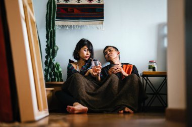 Genç bir Malay çift yatmak ve evlerinde sıcak bir içecek paylaşın. Onlar sarılır up ve birbirleriyle konuşmak gibi zemin ve rahat oturan.