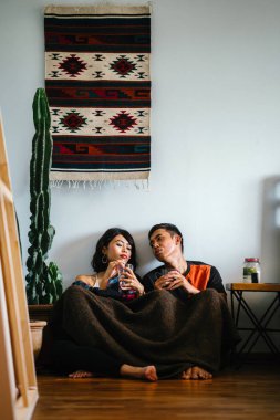 Genç bir Malay çift yatmak ve evlerinde sıcak bir içecek paylaşın. Onlar sarılır up ve birbirleriyle konuşmak gibi zemin ve rahat oturan.