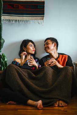 Genç bir Malay çift yatmak ve evlerinde sıcak bir içecek paylaşın. Onlar sarılır up ve birbirleriyle konuşmak gibi zemin ve rahat oturan.