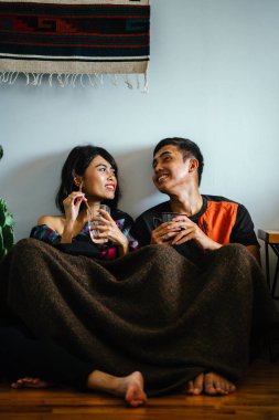 Genç bir Malay çift yatmak ve evlerinde sıcak bir içecek paylaşın. Onlar sarılır up ve birbirleriyle konuşmak gibi zemin ve rahat oturan.