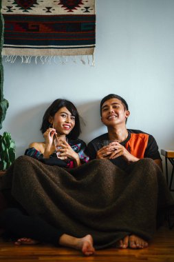 Genç bir Malay çift yatmak ve evlerinde sıcak bir içecek paylaşın. Onlar sarılır up ve birbirleriyle konuşmak gibi zemin ve rahat oturan.