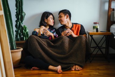 Genç bir Malay çift yatmak ve evlerinde sıcak bir içecek paylaşın. Onlar sarılır up ve birbirleriyle konuşmak gibi zemin ve rahat oturan.