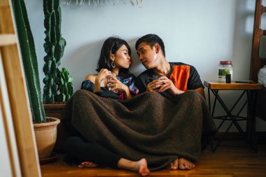 Genç bir Malay çift yatmak ve evlerinde sıcak bir içecek paylaşın. Onlar sarılır up ve birbirleriyle konuşmak gibi zemin ve rahat oturan.